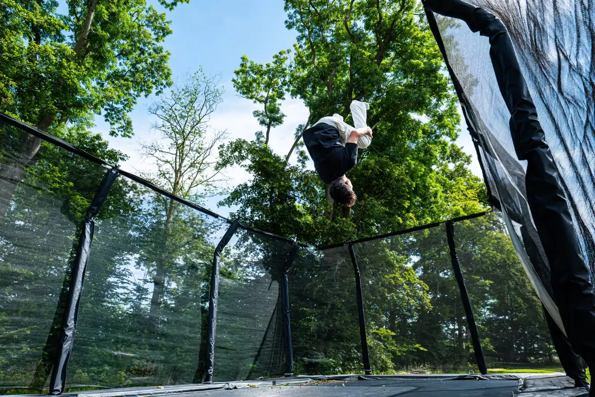 Trampolin i haven på Faurholt med træerne omkring